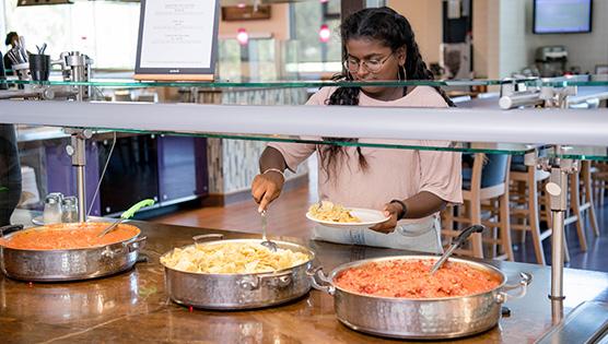 Student spooning out a serving of pasta from the self-serve area