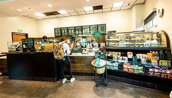 Student ordering at the counter of Starbucks next to a refrigerated case