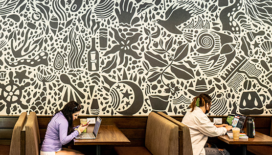 Black and white mural wall behind students sitting at booth tables in Starbucks