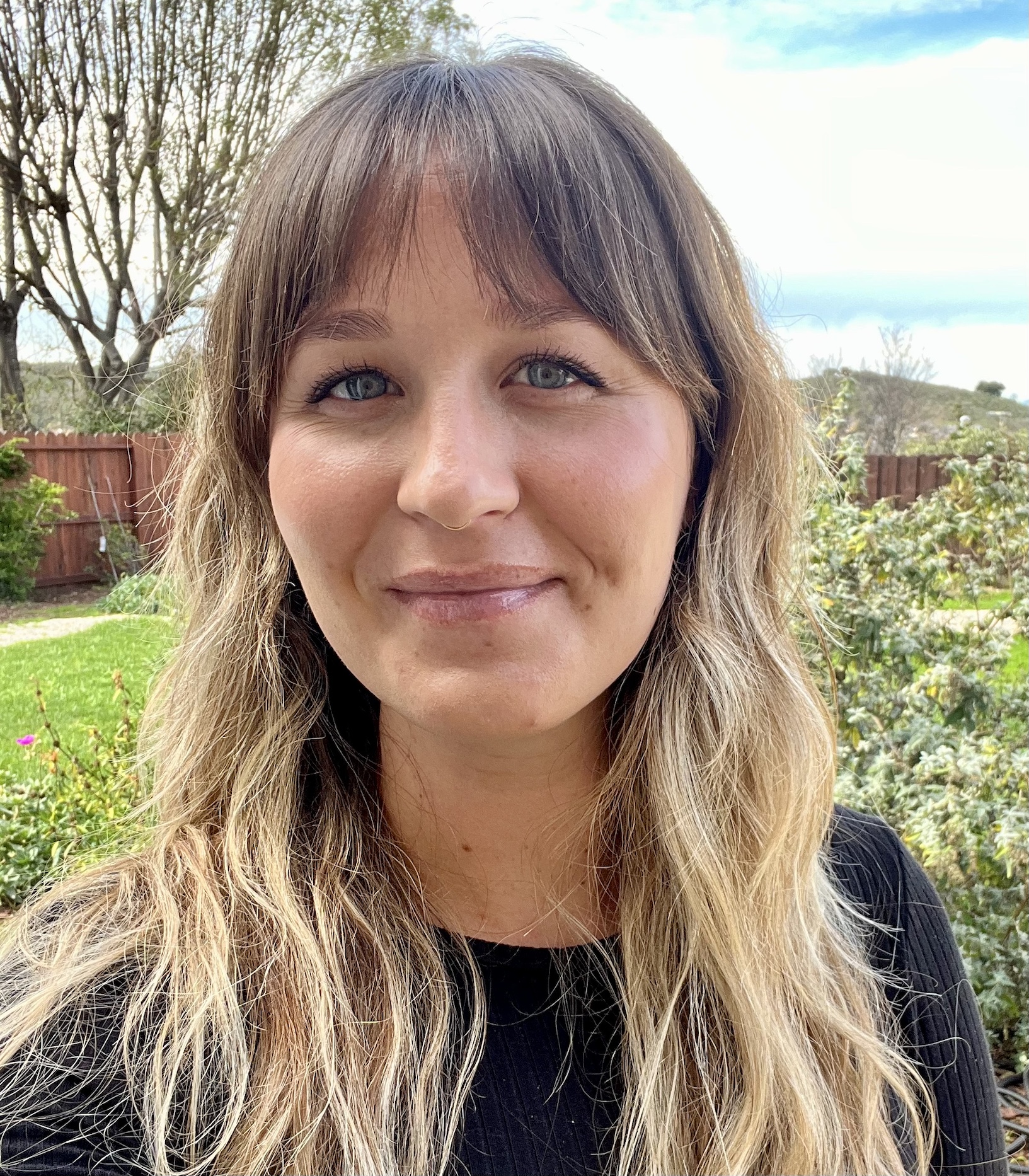 white woman with blue eyes and bangs in a black shirt